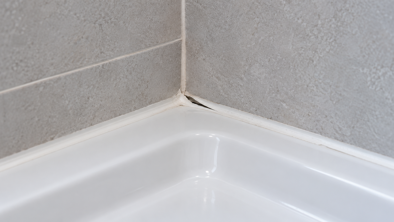 Silicone bianco staccato vicino all’angolo tra le piastrelle grigie e il piatto doccia.
